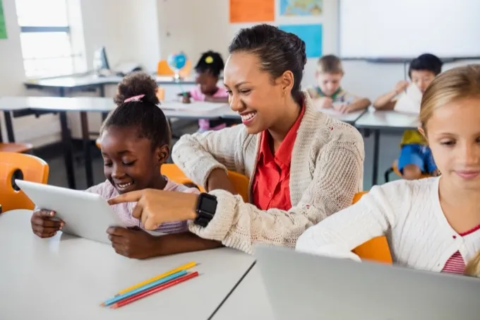 Teacher helping a student draw on a tablet in a classroom